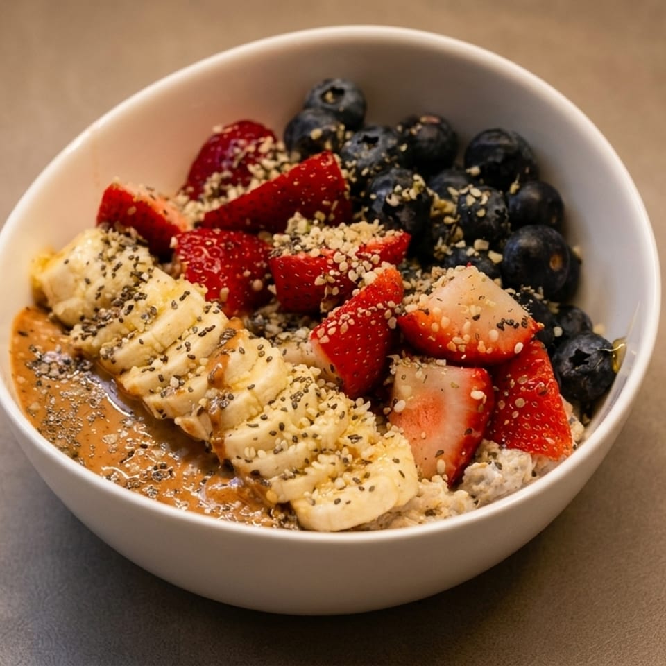 A white bowl filled with oatmeal, topped with sliced bananas, strawberries, blueberries, and seeds.